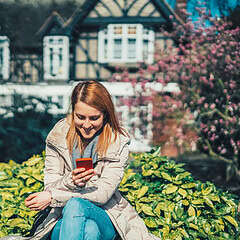 Woman using mobile phone outdoors, promoting savings with London Mutual Credit Union.