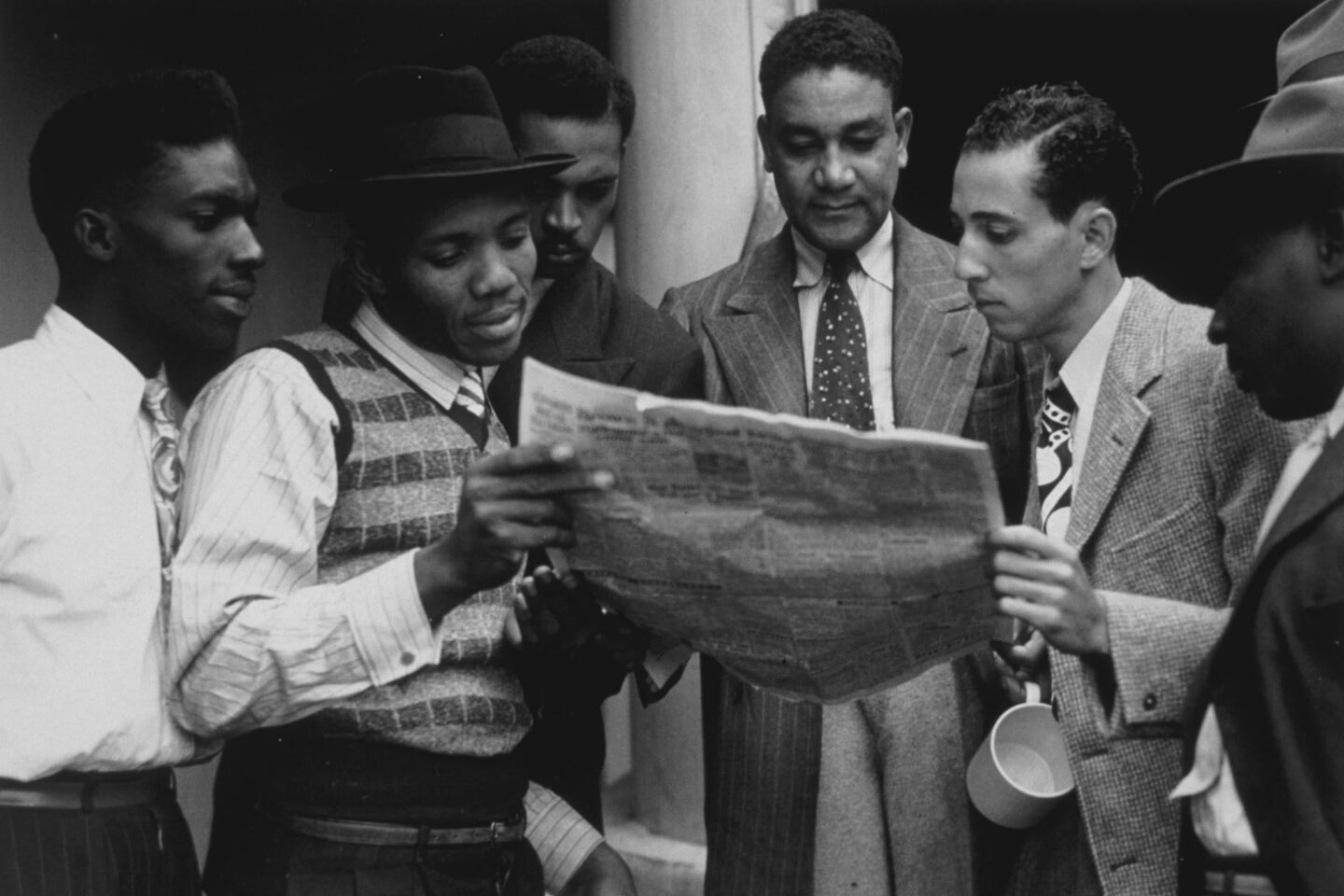 Historical photograph of smartly-dressed men looking at newspaper from around the same time as the arrival of Empire Windrush